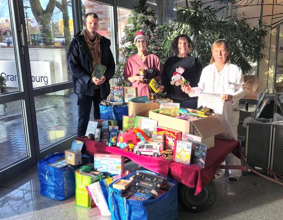 Bild im Foyer der Klinik Oranienburg: OHC-Geschäftsführer Martin Siegler übergab den Berg Spenden an Chefärztin Dr. med. Lucia Wocko (r.), Sarah Brockhausen, Leitende Oberärztin in der Tagesklinik für Kinder- und Jugendmedizin (2. v. r.) und Stationskoordinatorin Daniela Sachse (2. v. l., Foto: Oberhavel Kliniken/Odin Tietsche).